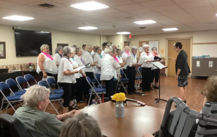 A choir of seniors performing indoors in front of an audience.