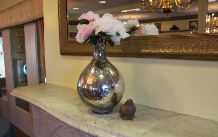 A decorative vase with flowers placed on a marble-topped table, reflecting in a mirror.