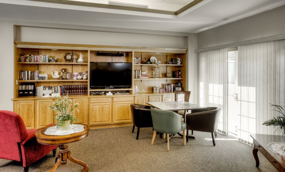 A cozy living room with a wooden bookshelf, television, and a small table surrounded by chairs.