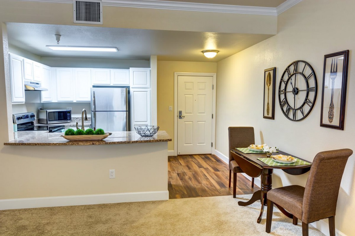 A modern apartment interior featuring a kitchen with a bar counter, a dining table, and wood flooring.