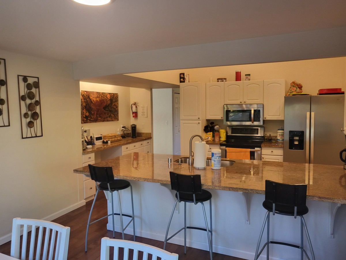 A modern kitchen with an open layout featuring a countertop with bar stools, appliances, and a cozy atmosphere.