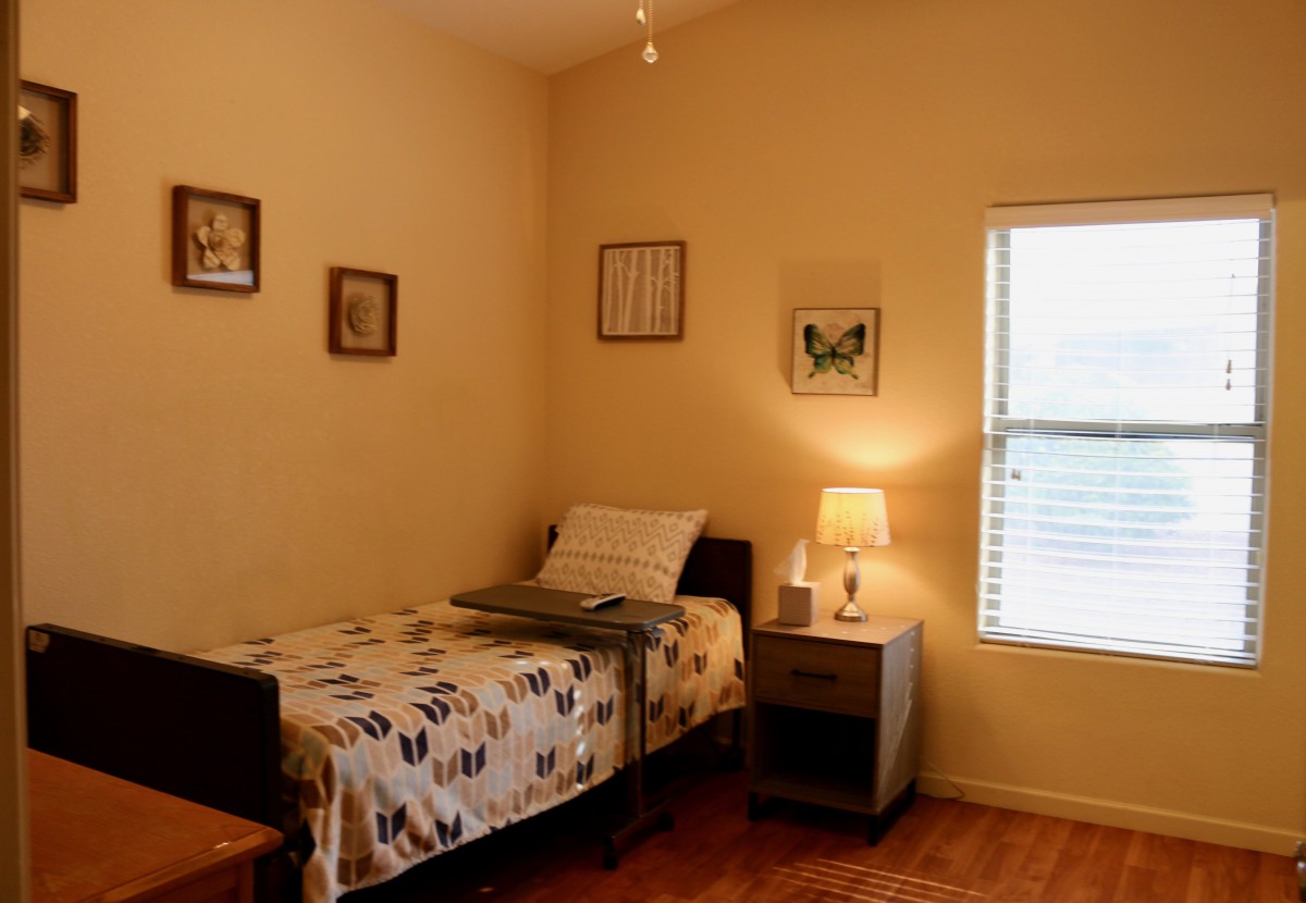 A cozy bedroom with a single bed, nightstand, and soft lighting from a lamp beside the window.