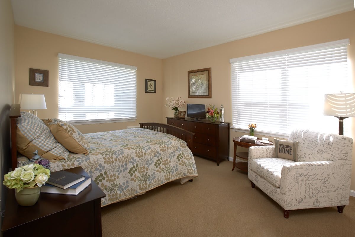 A cozy bedroom with neutral tones, featuring a bed, dresser, and armchair.