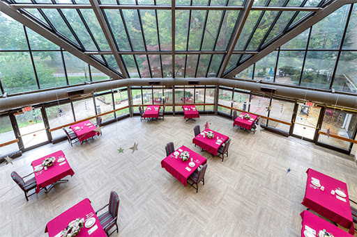 A spacious dining area with red tablecloths and large glass windows offering a view of the surrounding nature.
