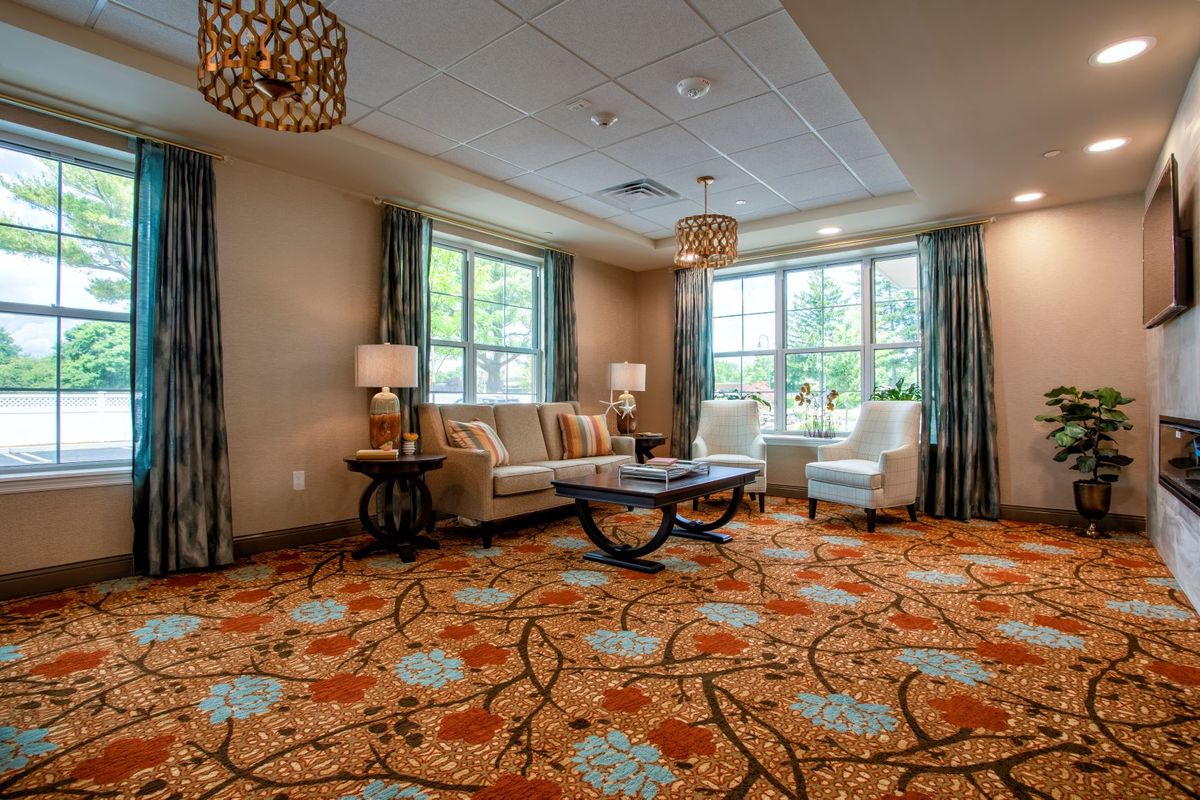 A cozy living room featuring a patterned carpet, comfortable seating, and large windows allowing natural light.
