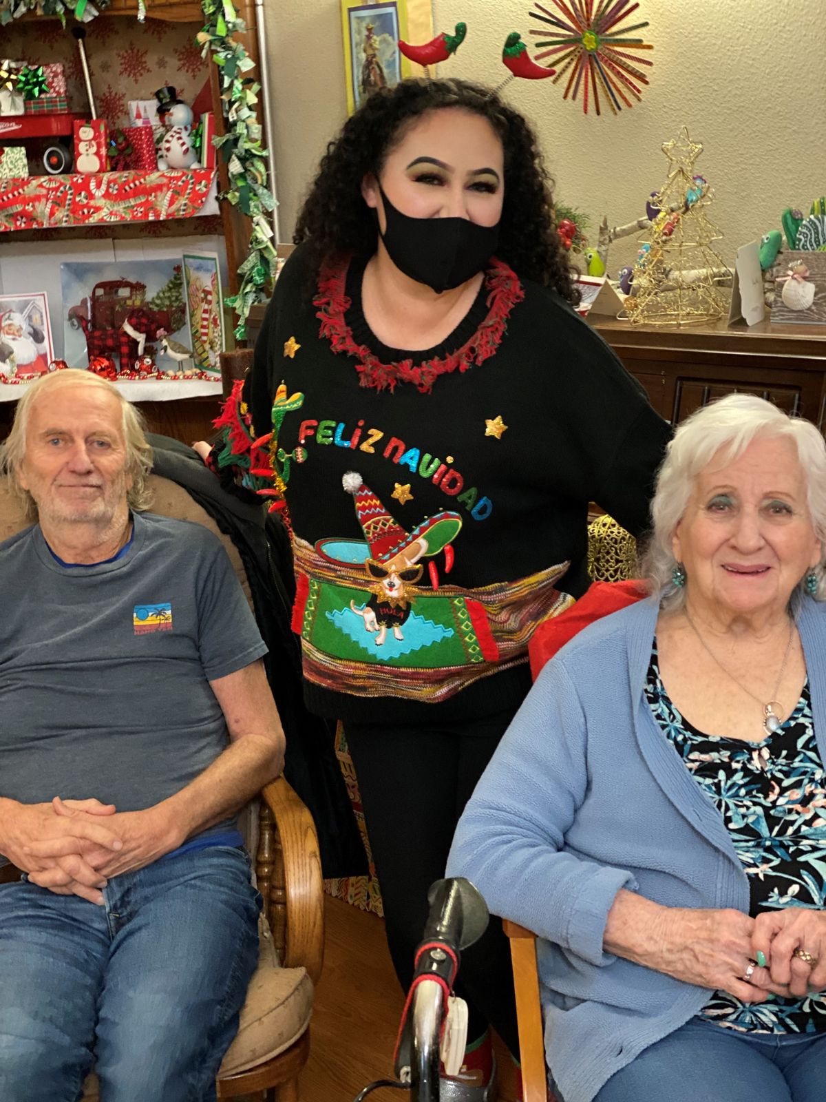 A festive holiday gathering with three people, including a person wearing a Christmas sweater and mask.