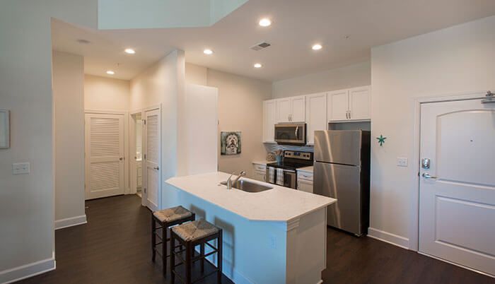 A modern kitchen with white cabinetry and stainless steel appliances, featuring a central island with bar stools.