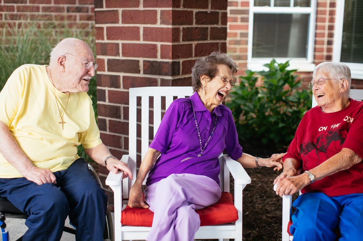 A group of elderly people sitting outdoors, enjoying a lively conversation and laughing together.