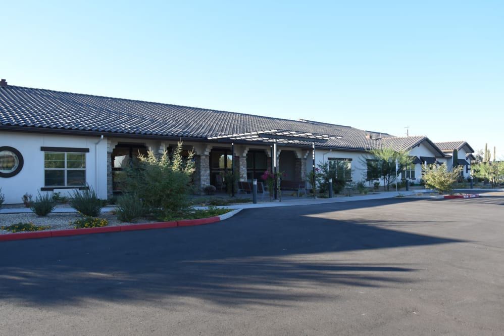 A single-story building with a tiled roof, surrounded by greenery and adjacent to a parking area.