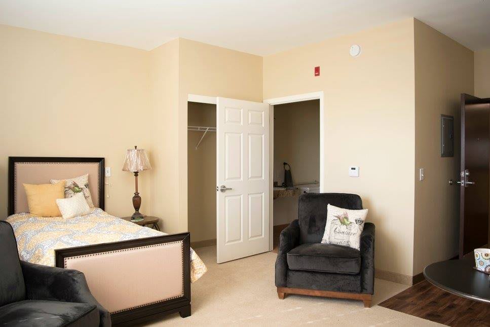 A cozy bedroom with a bed, an armchair, and an open closet door.