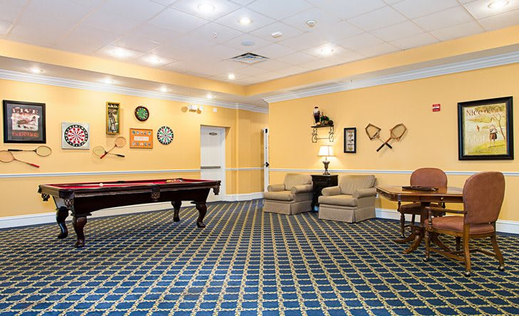 A cozy game room featuring a pool table, shuffleboard, and comfortable seating with wall decorations.