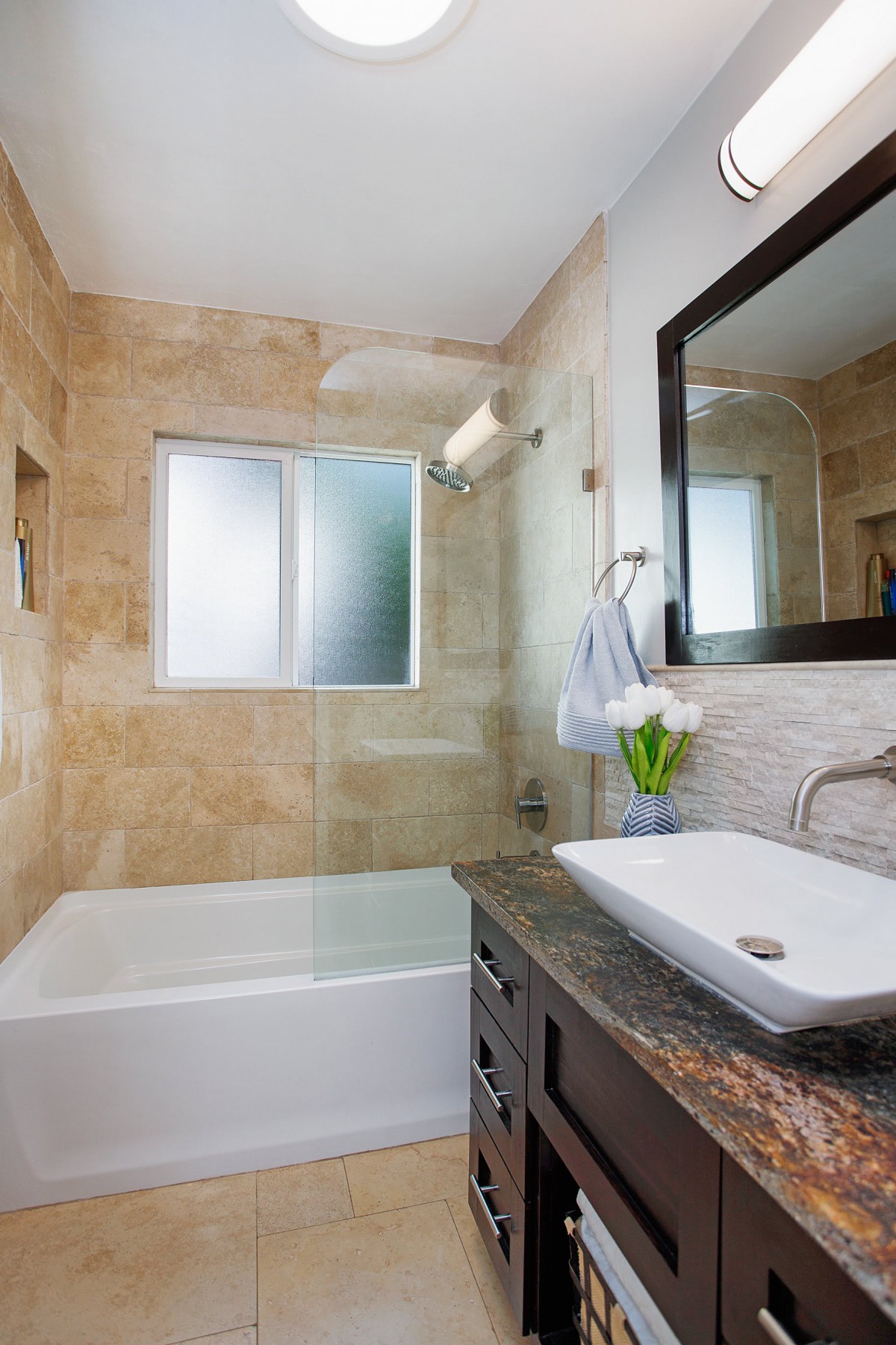 A modern bathroom featuring a sleek sink, bathtub, and large mirror with neutral tile accents.