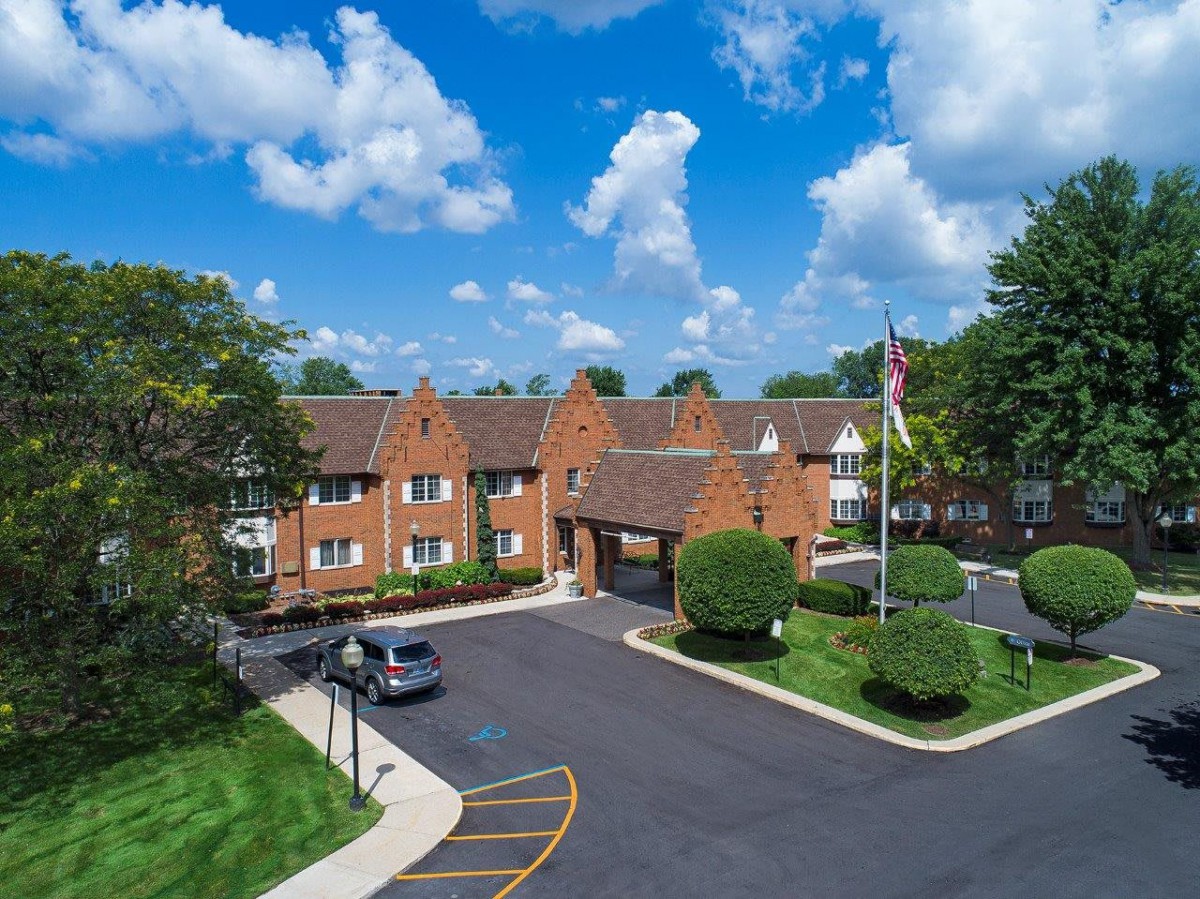 A brick building with a sloped roof and an adjacent parking lot under a partly cloudy sky.