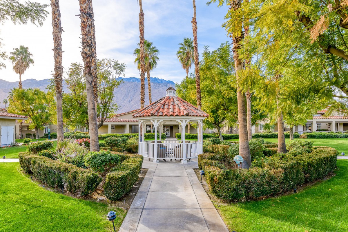 A charming gazebo surrounded by lush greenery and towering palm trees, set against a backdrop of mountains.