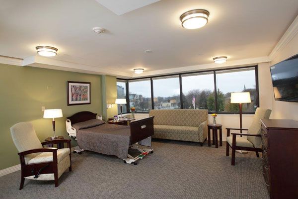 A well-lit hospital room featuring a bed, sofa, and large windows.