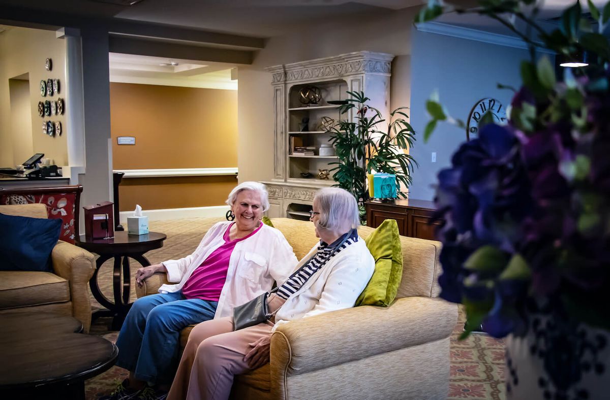 Two elderly women sitting on a couch, engaging in conversation in a cozy living room setting.