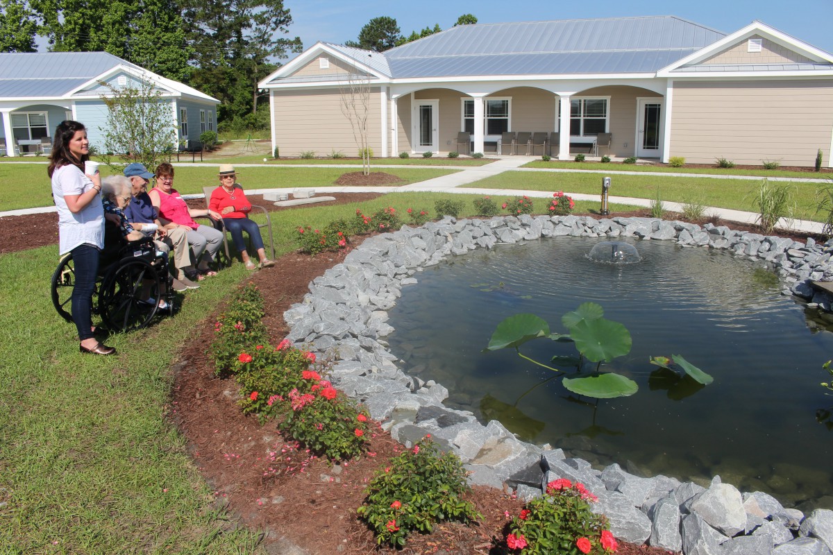 A group of people sitting by a landscaped garden with a pond in front of a house.
