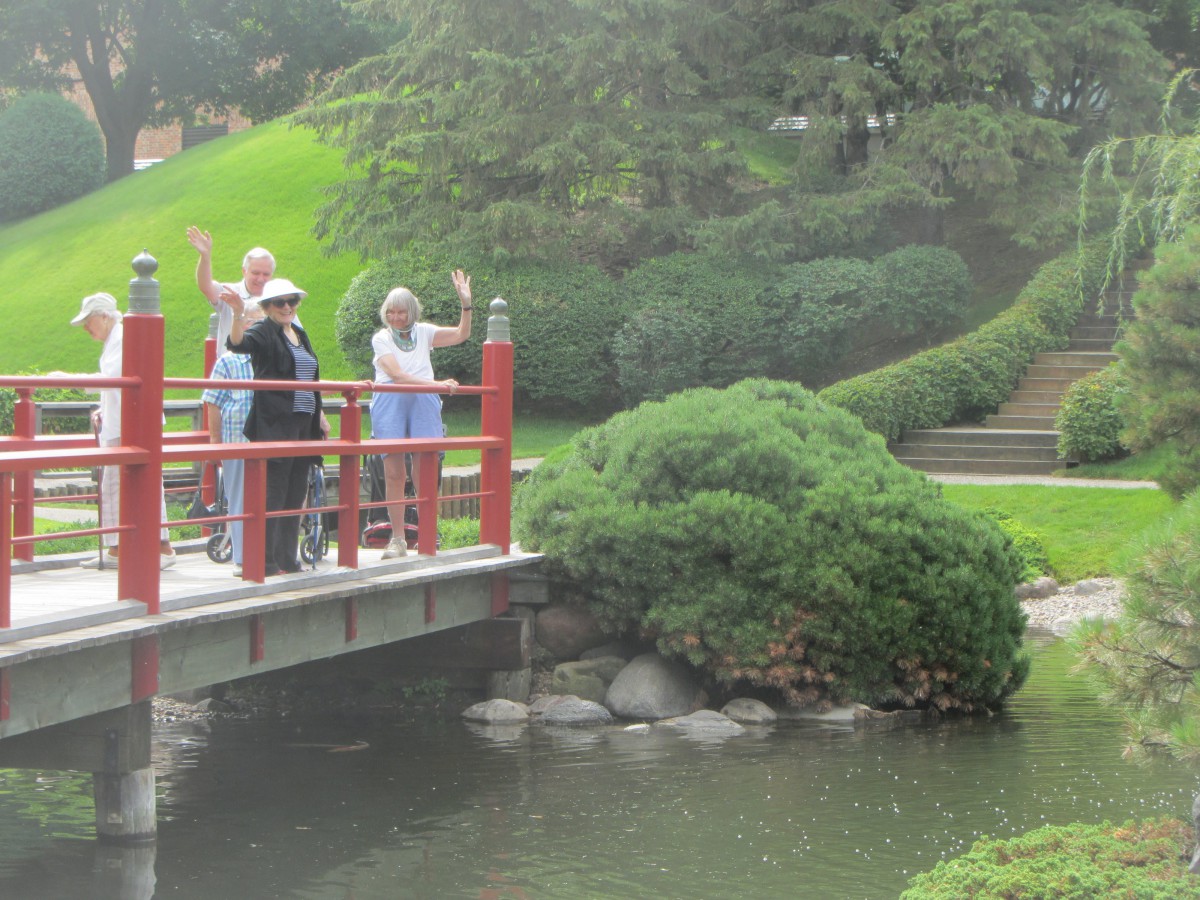 A group of people waving while standing on a bridge in a lush garden.