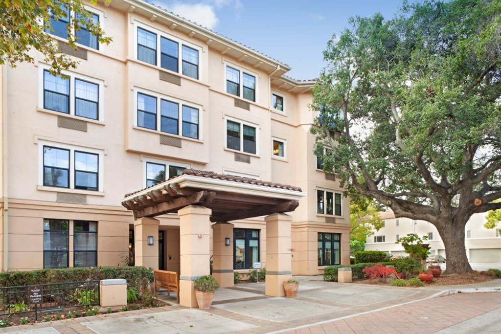 A four-story residential building with a covered entrance and surrounding trees.