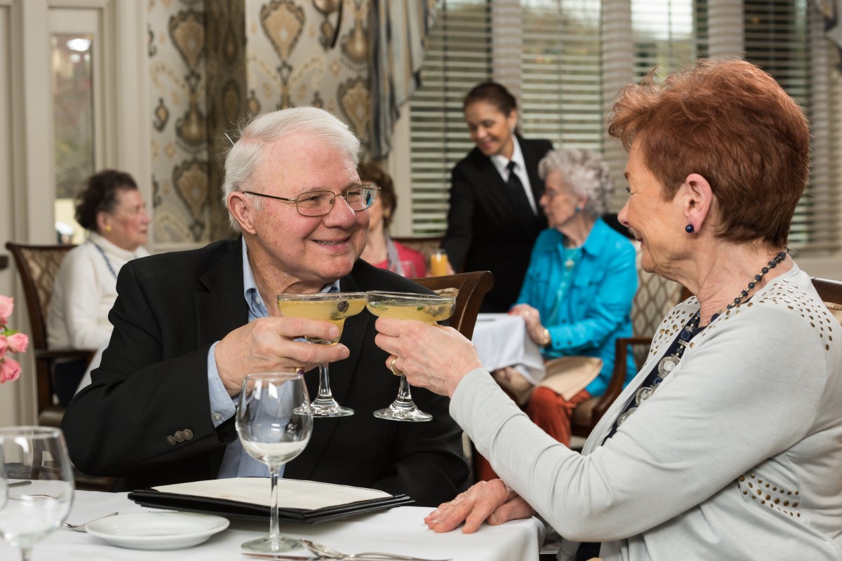 A senior couple is enjoying a celebratory toast at a restaurant, served by attentive waitstaff.