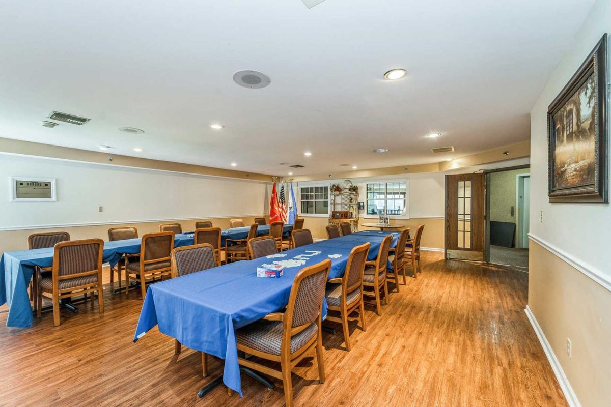 A spacious meeting room with blue tablecloths covering long conference tables surrounded by chairs, featuring a wooden floor and interior lighting.