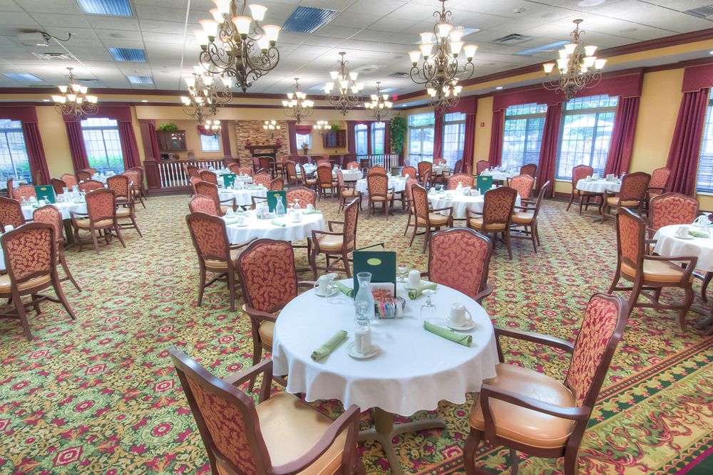 A beautifully arranged dining room with elegant chandeliers, round tables set for meals, and a plush carpeted floor.