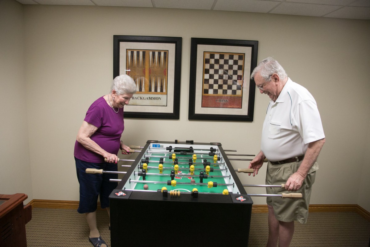 Two elderly individuals enjoy a game of foosball together indoors.