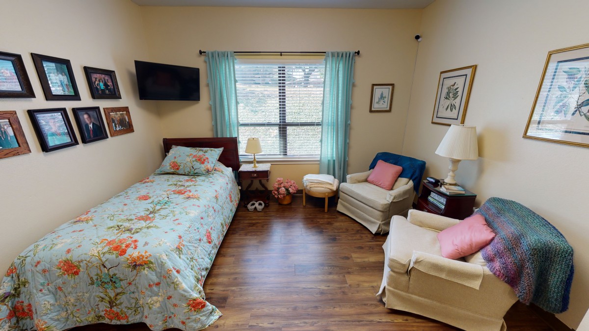A cozy bedroom featuring a single bed, two armchairs, and a TV, with natural light streaming through the window.