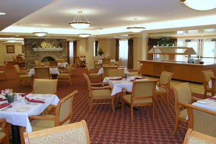 A spacious dining area with neatly arranged tables and chairs, featuring a warm, carpeted floor and elegant chandeliers.
