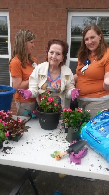 A group of people enjoying a gardening activity, planting flowers in pots outdoors.