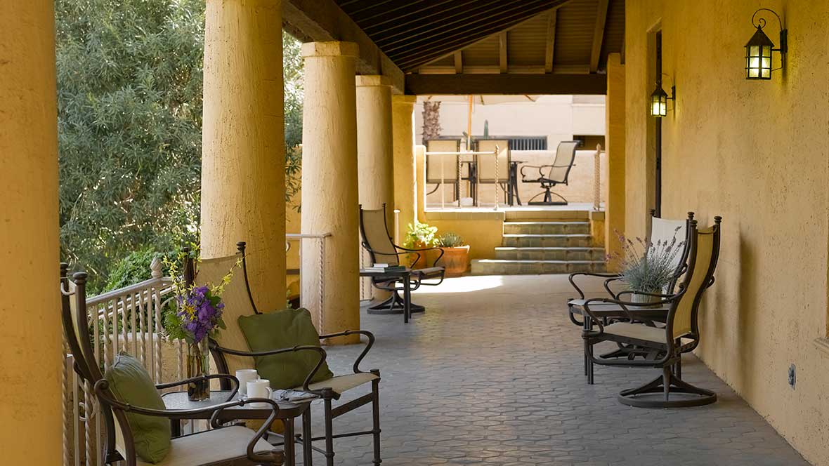 A serene patio with chairs and tables, shaded by a column-supported roof.