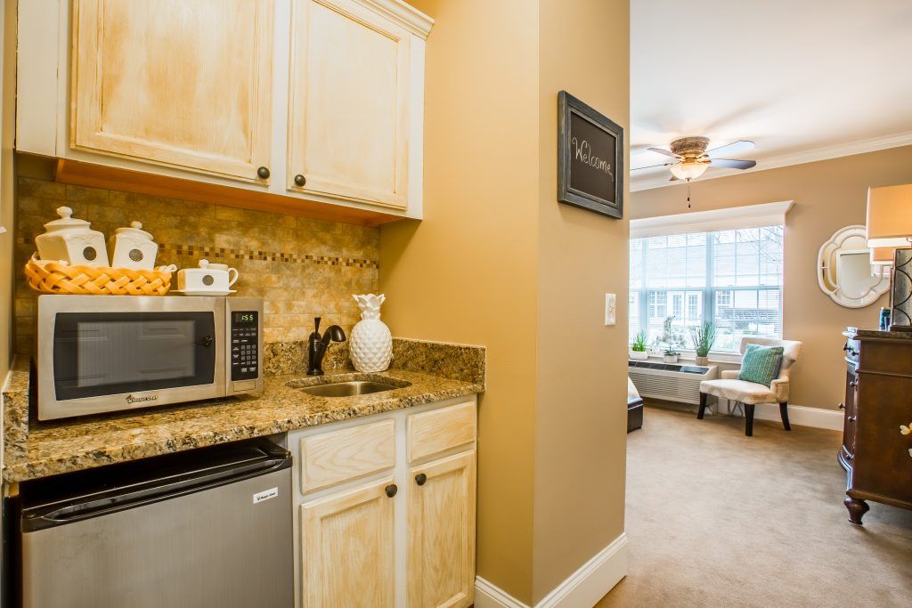A cozy kitchenette area with a microwave, mini fridge, and granite countertop leading into a bright living space.