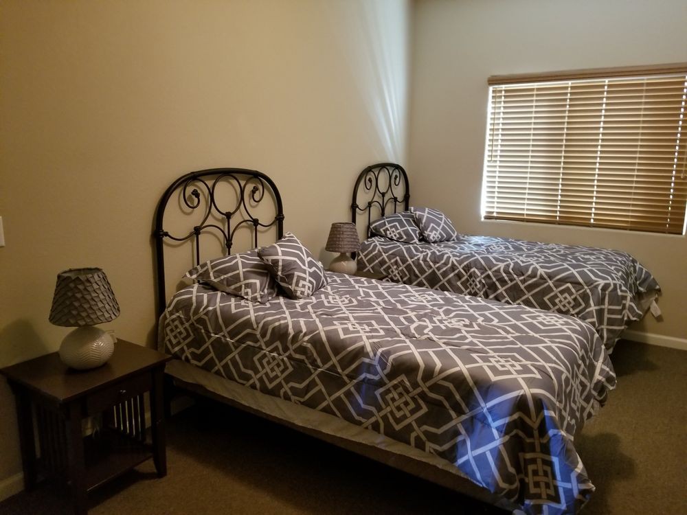 A bedroom with two twin beds featuring patterned bedspreads, a nightstand with a lamp, and a window with blinds.