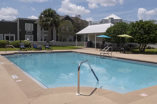 A sunny day at a residential outdoor swimming pool with a patio area.