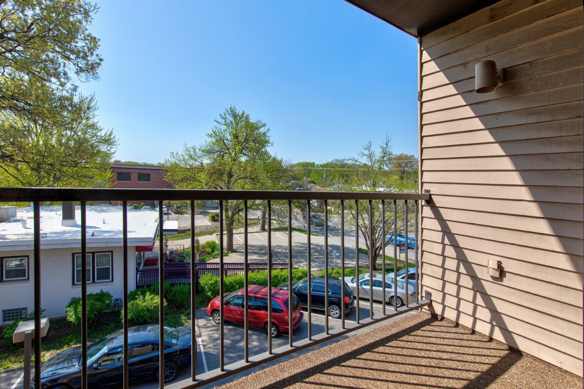 View from a balcony overlooking a parking lot and trees in a residential area.