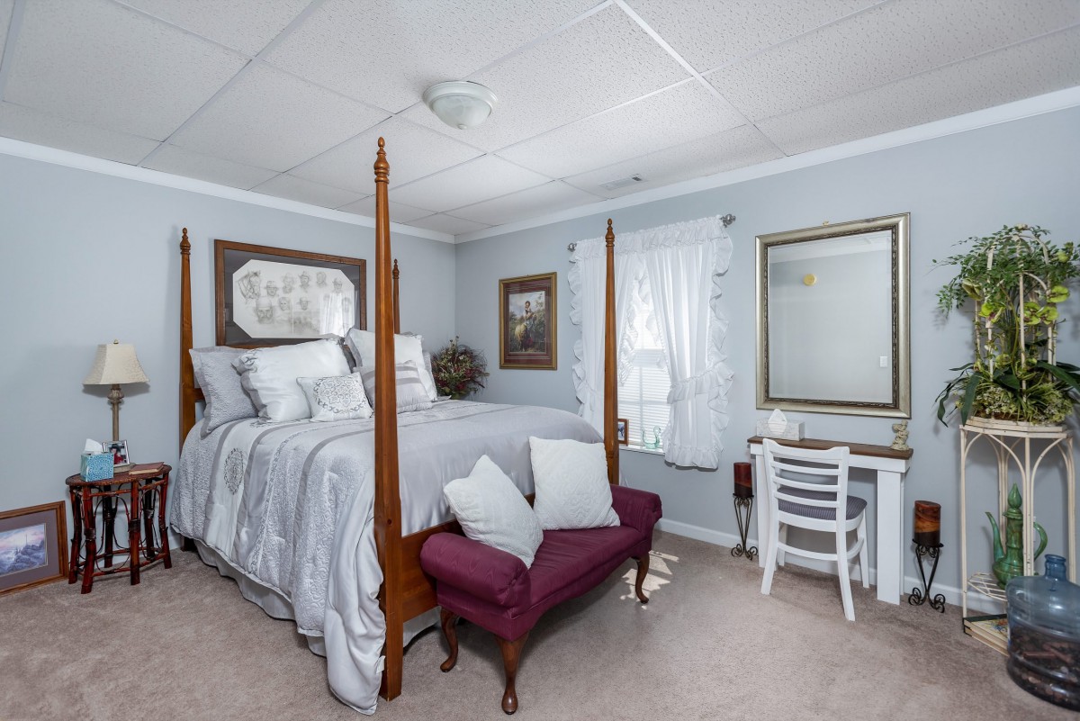 A cozy bedroom with a four-poster bed, desk, and mirror, featuring light blue walls and elegant decor.