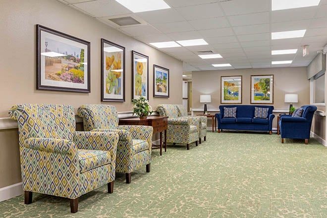 A well-lit waiting room with patterned chairs, a blue sofa, and landscape paintings on the walls.