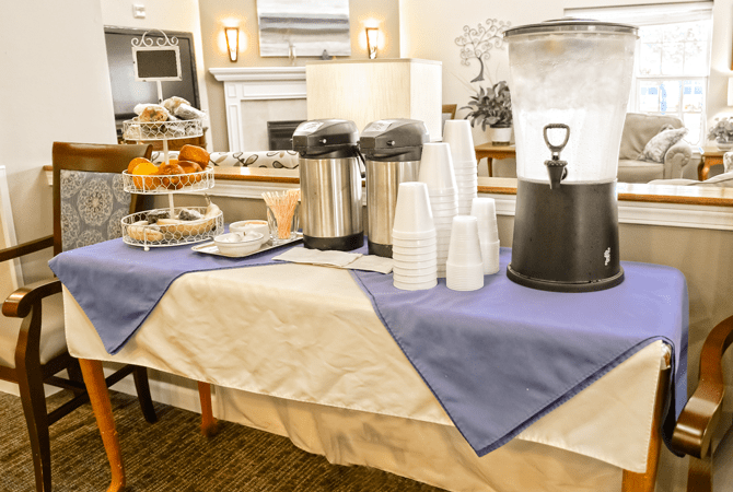 A coffee and snack station set up for an event, featuring coffee dispensers, cups, a water cooler, and a selection of pastries.