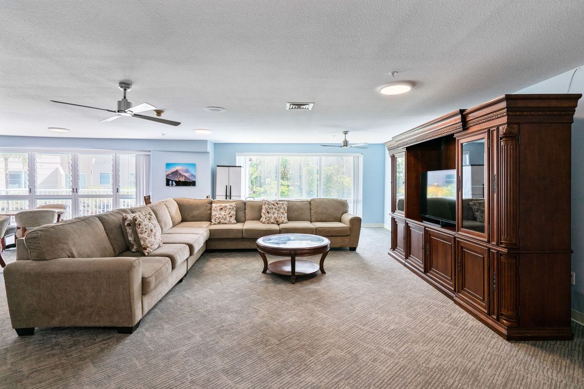 A spacious living room with a large sectional sofa, coffee table, and entertainment center, beautifully lit by natural light streaming through the windows.