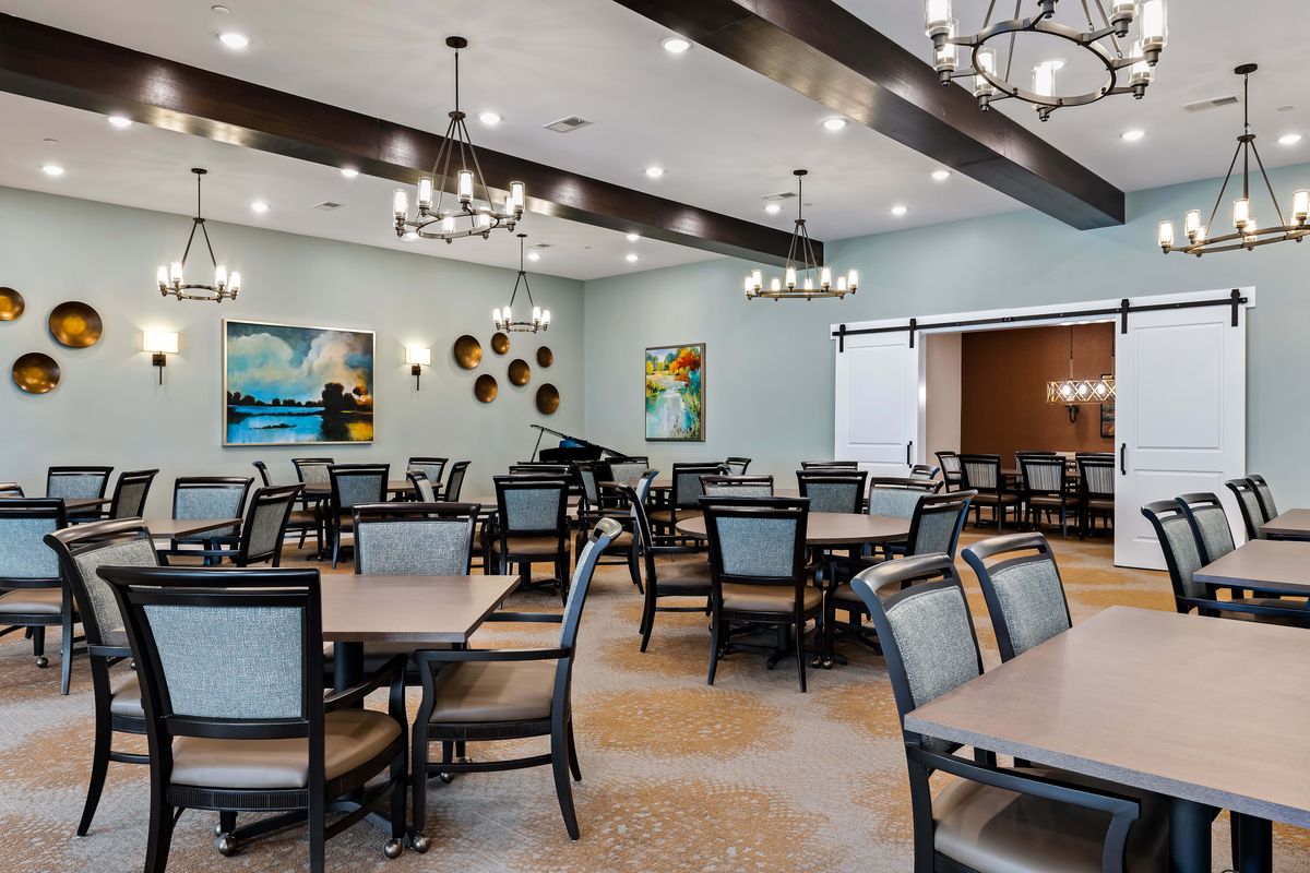 A spacious dining room with elegant chandeliers, neatly arranged tables and chairs, and decorative artwork on the walls.