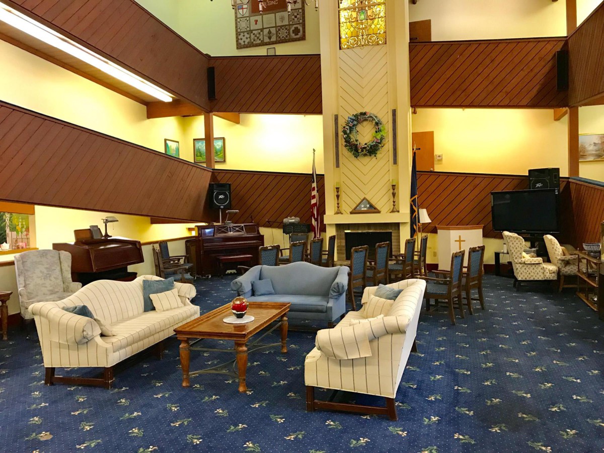 A cozy lounge area featuring sofas, a coffee table, and a piano, centered around a fireplace.