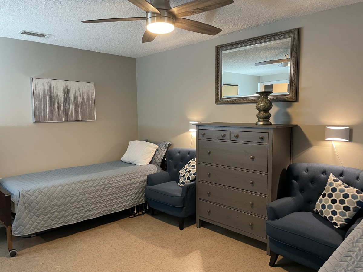 A cozy bedroom featuring a single bed, gray dresser, comfortable armchairs, and stylish decor.