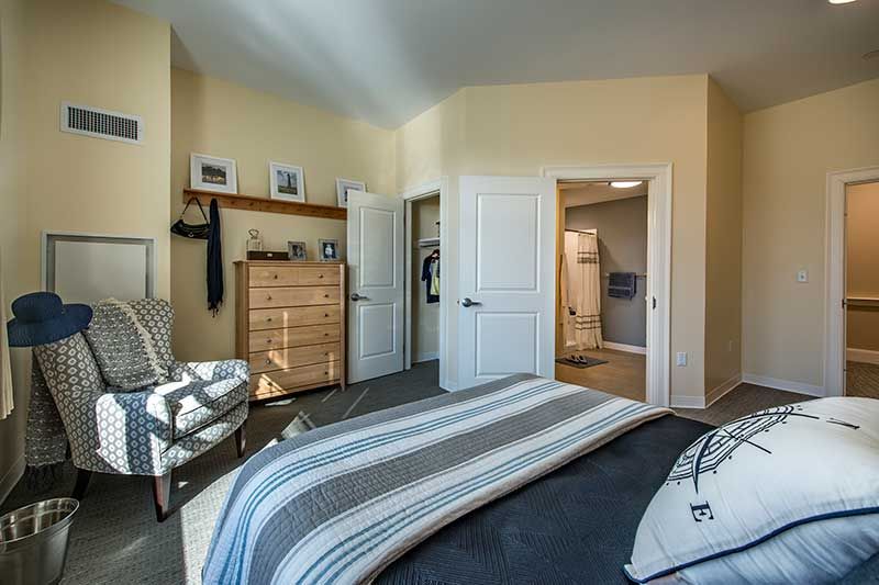 A cozy bedroom with a striped bedspread, dresser, and open closet.