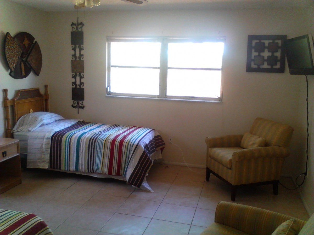 A cozy bedroom with a bed, chair, and window letting in natural light.