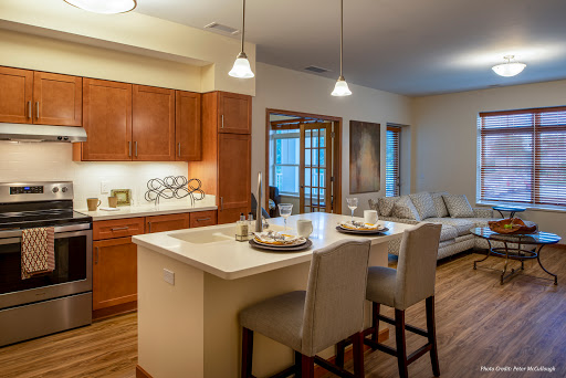 A stylish open-concept kitchen and living area featuring wooden cabinetry, modern bar stools, and inviting lighting.