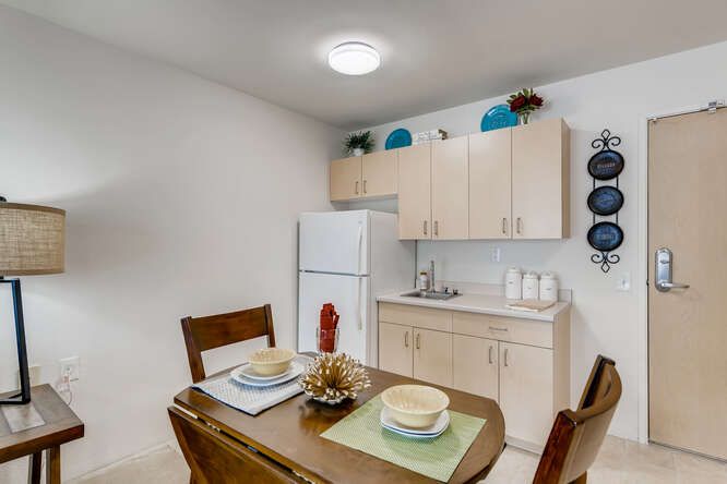 A cozy kitchen and dining area featuring a wooden table set with plates and cups, complemented by light-colored cabinets and a refrigerator.