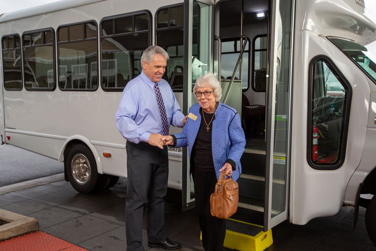A man assists an elderly woman as she steps off a bus.