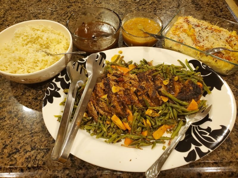 A dinner spread featuring a platter of grilled meat with vegetables, mashed potatoes, and sauces.