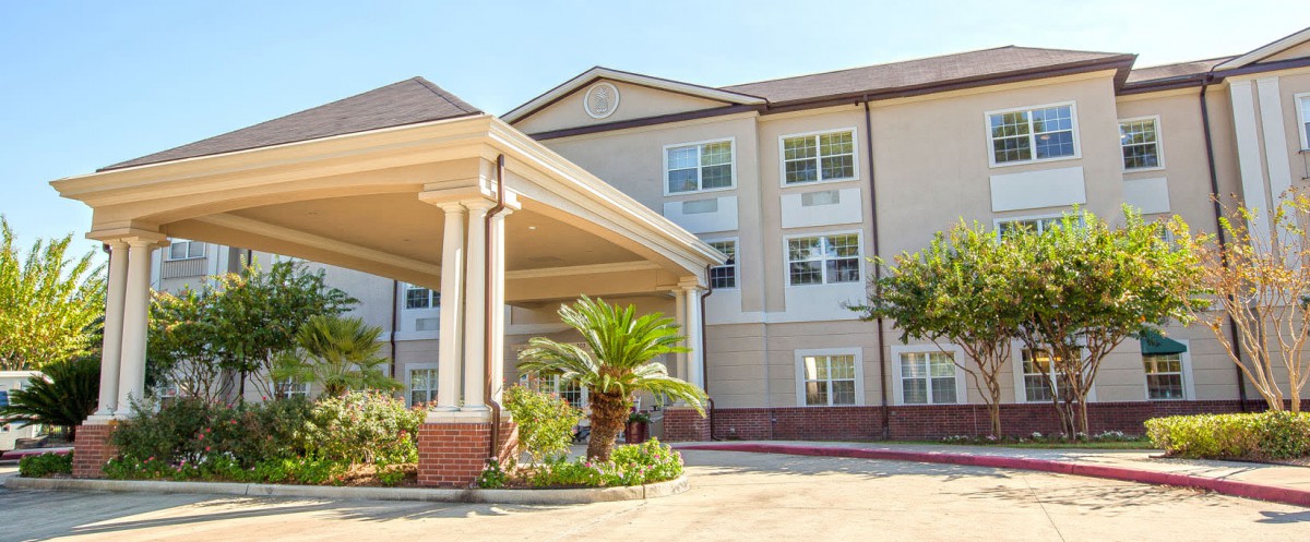 A modern hotel building with a covered entrance and palm trees in front.