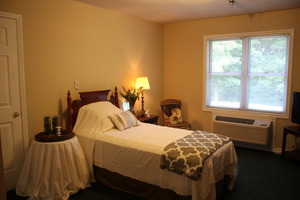 A cozy bedroom featuring a neatly made single bed, with warm lighting and a window overlooking greenery.